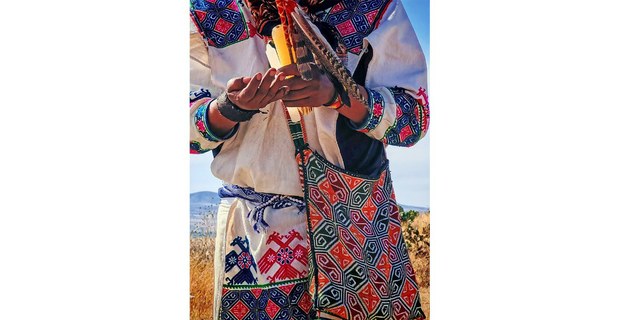 Integrante wixarika sostiene una vela y elementos rituales en la inauguración del Xiriki, acompañada por fuego, cantos y agradecimientos en Makwipa